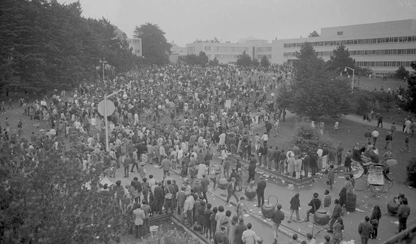 Aerial view of a crowd marching along a paved road. It appears to be a protest.