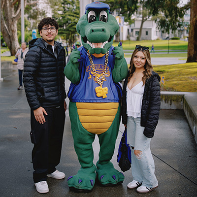 Two people pose for a picture with the Alli Gator mascot outside on campus