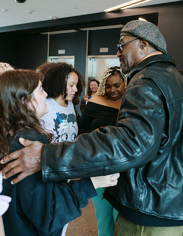 Delroy Lindo embraces several students while they smile and stand in the hallway of the SFSU Science and Engineering Innovation Center