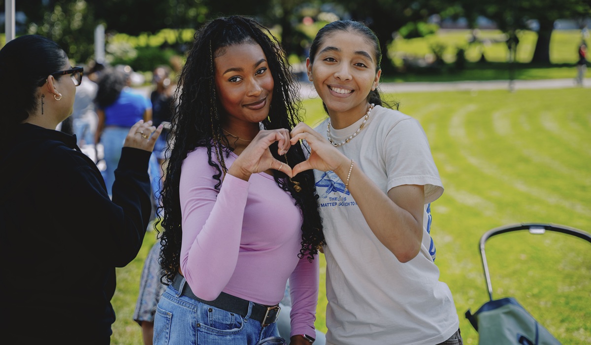 Two female students make a heart shape with their hands