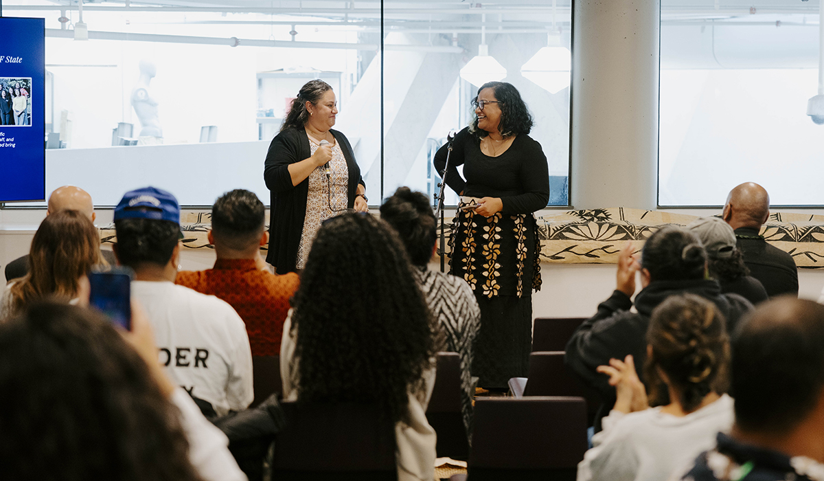 Two people standing in front of an audience that is sitting down.