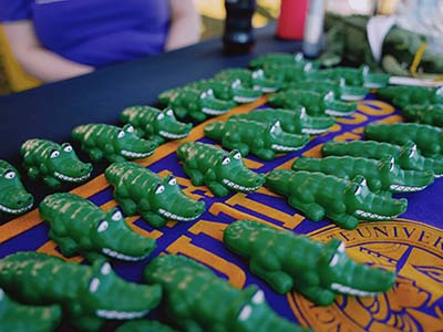 Small toy SFSU Gator mascots are placed on a San Francisco State University tablecloth in three rows