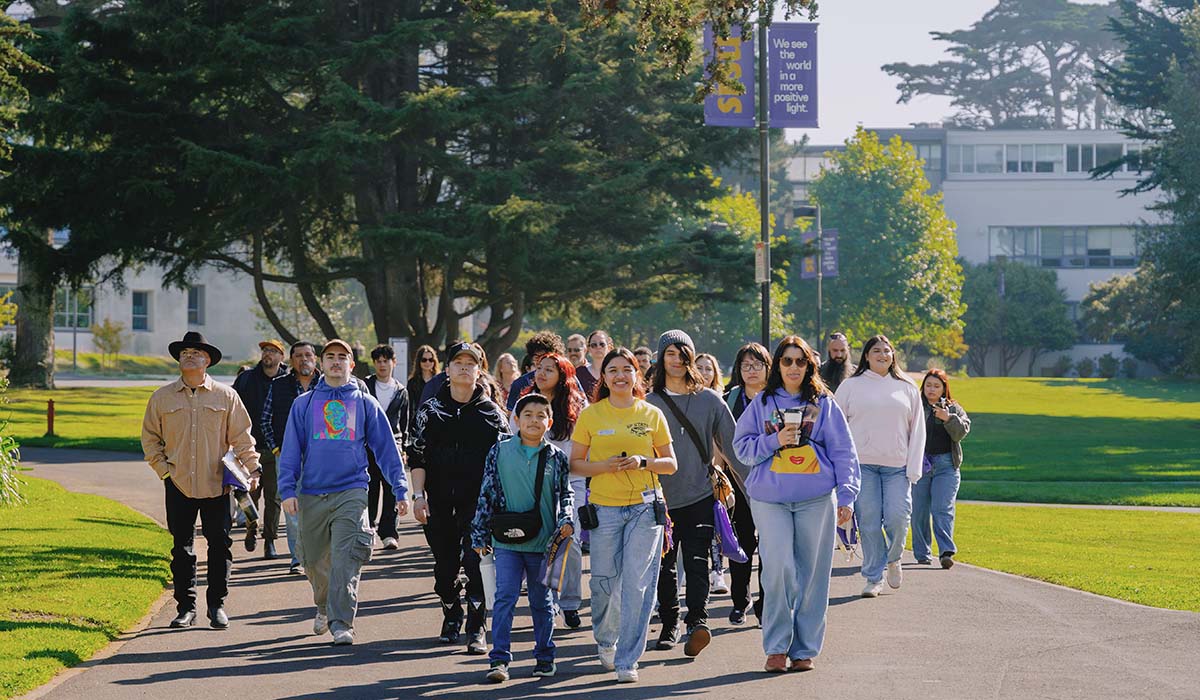 A student tour guide leads future SFSU students and families on a walk through the Quad on a sunny day 