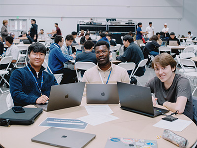 Three students with laptops smiling at the camera