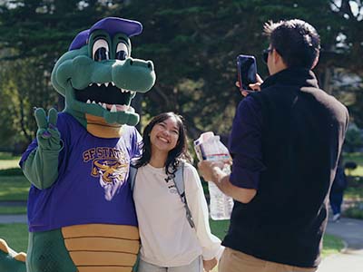 A person taking a photo of a smiling student and Alli Gator who is making a peace sign