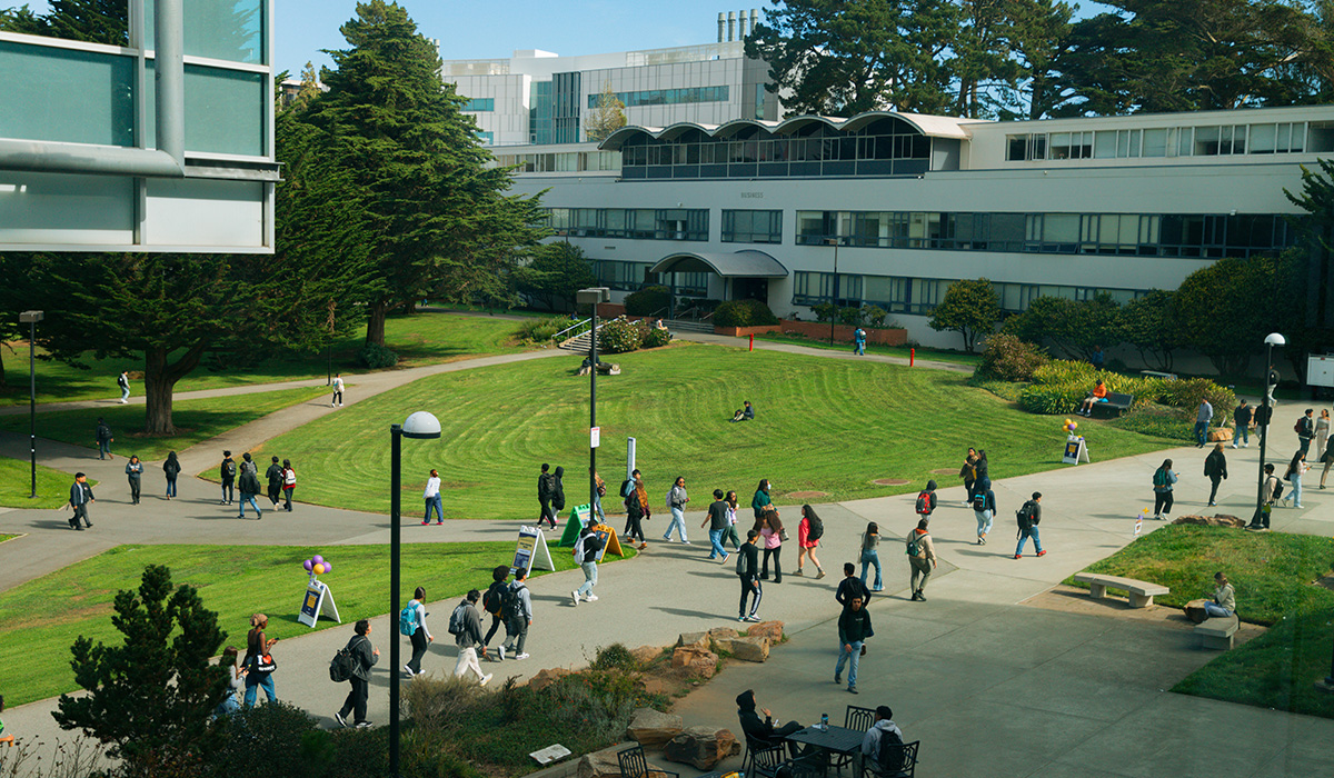 Students and others walk through the SFSU Quad, J. Paul Leonard Library and Business building