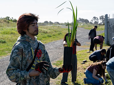 Student holding a pot with a tall grass-like plant