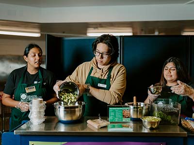 Three people pouring vegetables into a giant bowl