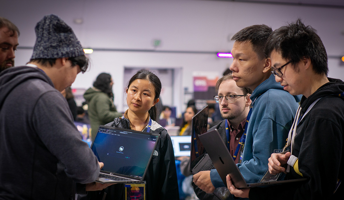 At the SF Hacks event, six people stand in a huddle while holding laptop computers