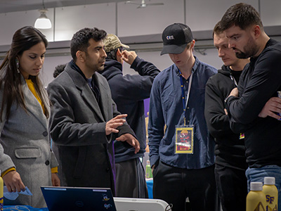 At the SF Hacks event, four people engage in a discussion while standing in front of a table with an open laptop computer