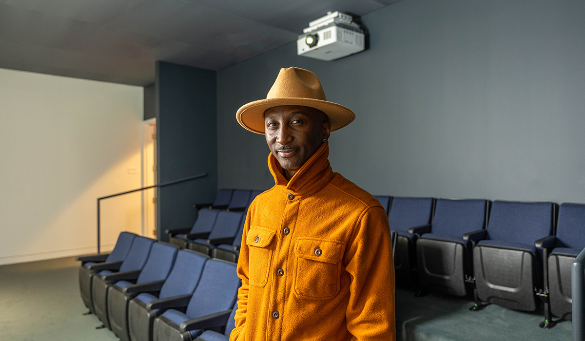 Artel Great stands in a screening room wearing an orange hat and orange collared shirt