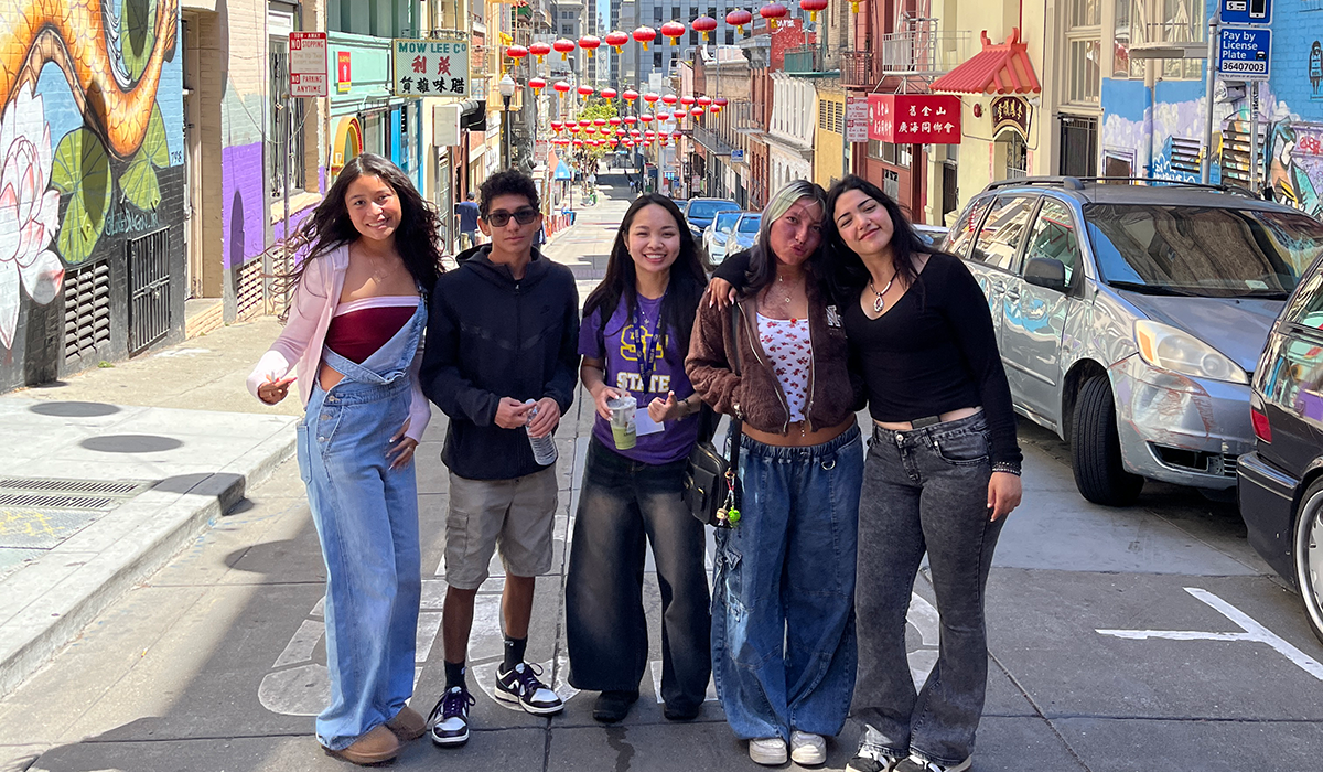 Five students pose for a photo while standing in a street in the Chinatown neighborhood of San Francisco on a sunny day