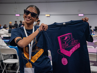 A person wearing sunglasses holds up an SF Hacks T-shirt while at the event