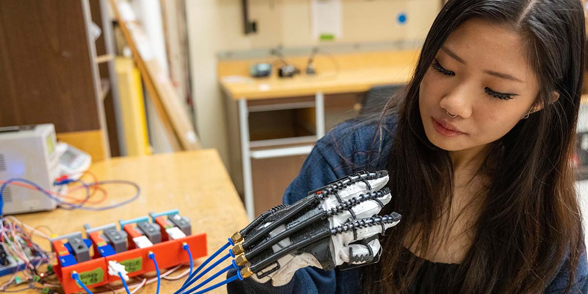Lauren Gan wears and looks at her exoskeleton glove