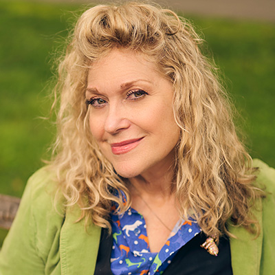 A person with blonde shoulder length hair wearing a light green sweater smiles