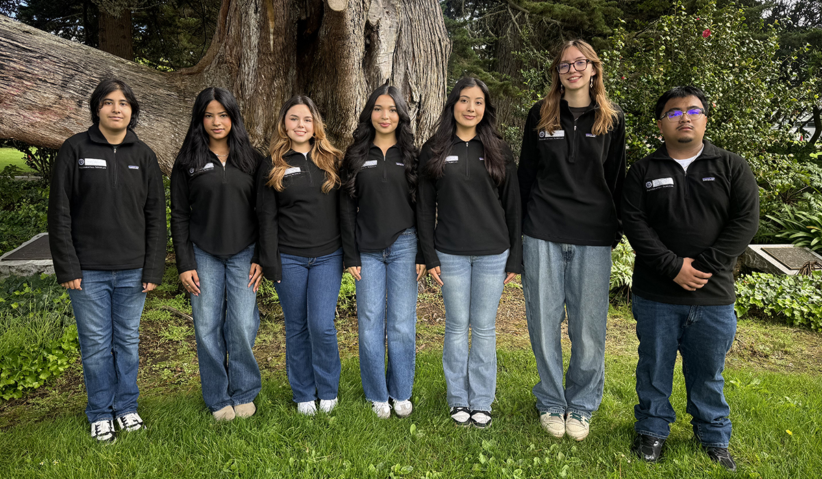 A group of students standing in a line posing for the camera with trees in the background.