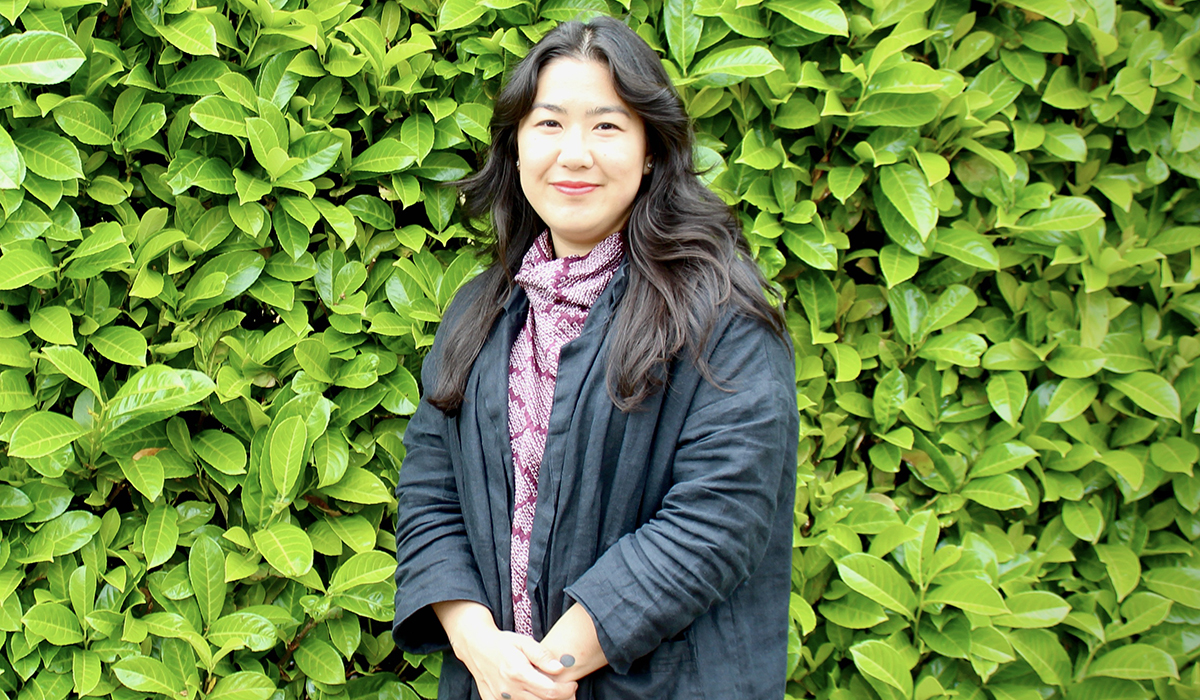 A woman smiling with green foliage in the background.