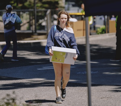 A female student walks with a cardboard box
