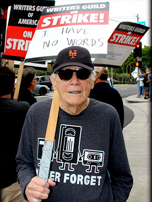 David Pollock marches on the picket line with a sign reading Writers Guild of America on Strike! with handwritten text I Have No Words