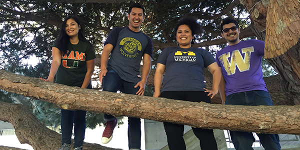 Four students standing in a tree wearing college t-shirts