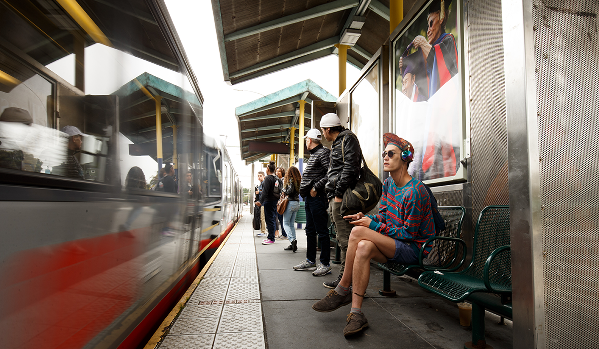 People sit at the SF State/Parkmerced Muni station while a train is stopped