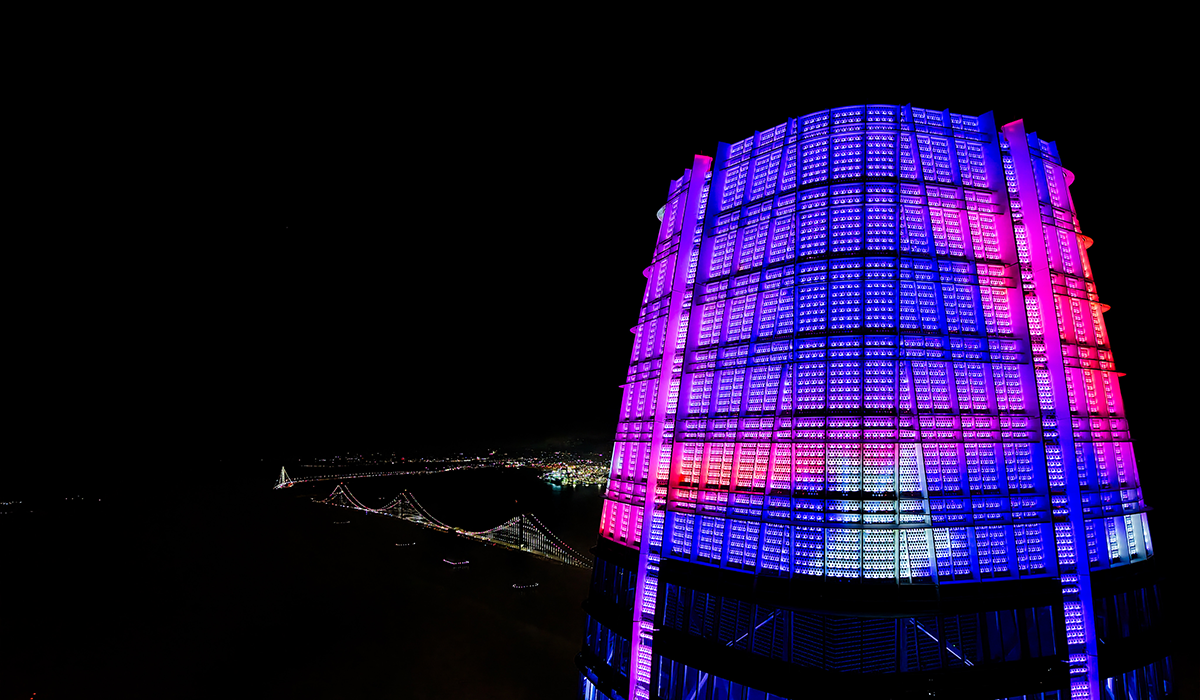 A drone photo of the top of the Salesforce Tower in San Francisco showing colorful SFSU student artwork with the Bay Bridge visible in the background
