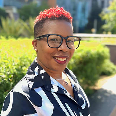 a person with short red cropped hair and dark glasses smiles 