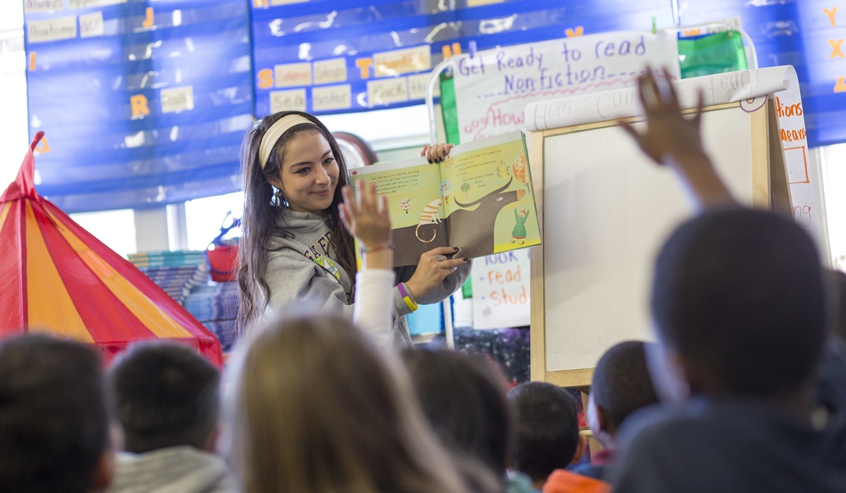 A student reads to children in a classroom