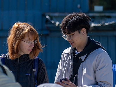 Two students stand next to each other outdoors while one of them holds a sea urchin