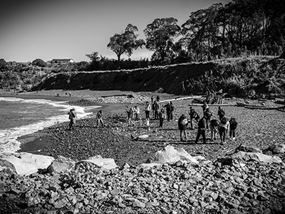 A black and white photo of people in an SFSU class standing on the sand at a beach near a cliff