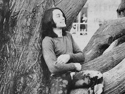 A black and white photo of Charles Thorpe smiling while sitting in a tree on campus wearing a long-sleeve shirt and bleached pants