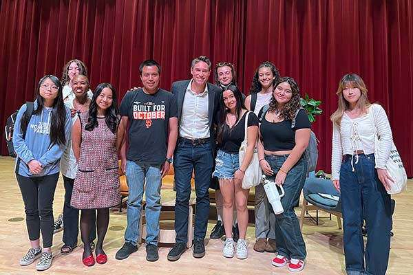 Whit Johnson, Venise Wagner and nine students smiling on a stage