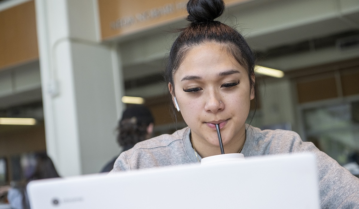 A woman sucks on a straw while looking at a laptop