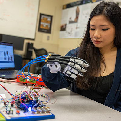 student wearing and looking at a bionic hand