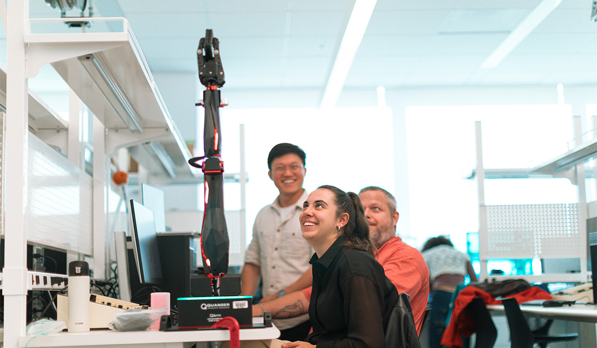 three students looking at a fully extended robotic arm