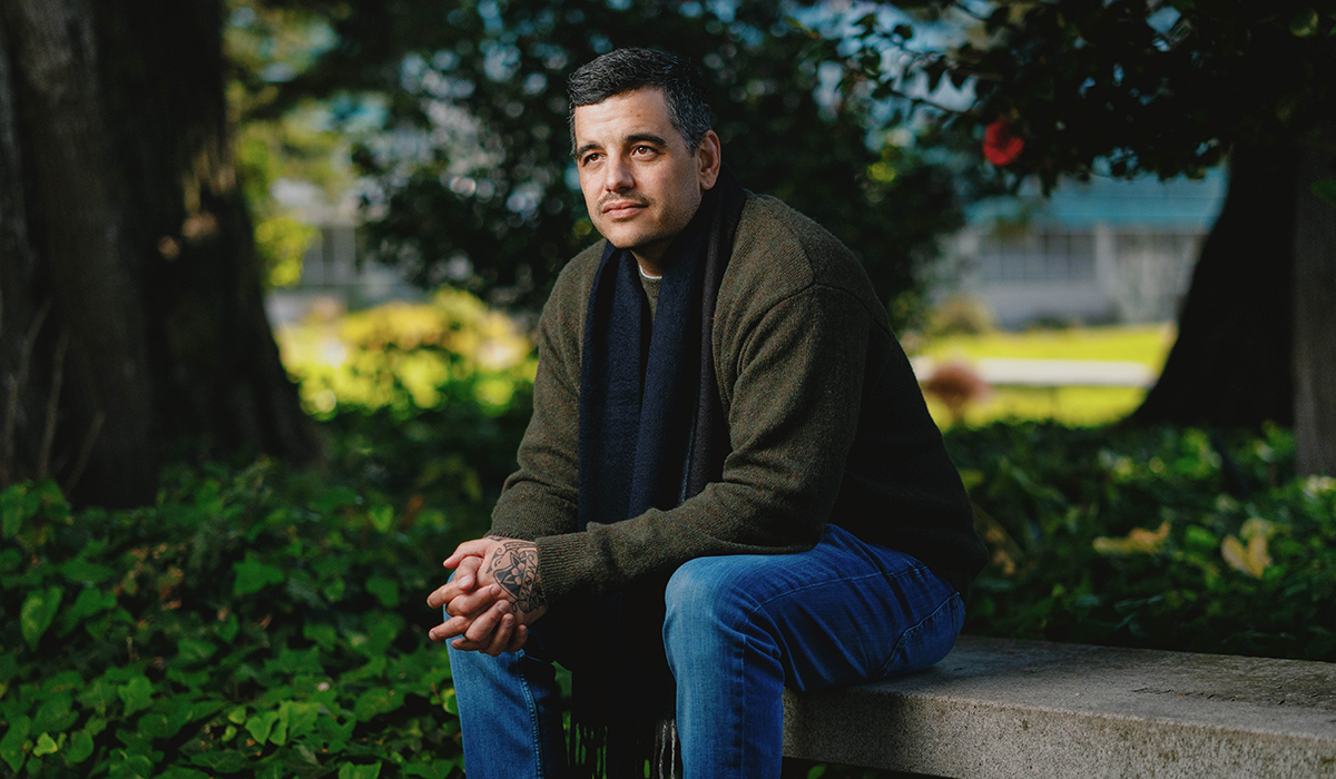 Man in olive green jacket and jeans sitting on a concrete bench.
