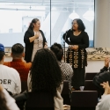 Two people standing in front of an audience that is sitting down.