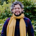 Personal smiling against green foliage in the background.