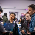 At the SF Hacks event, six people stand in a huddle while holding laptop computers