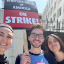 From left: Lecturer Marion Dayre takes a selfie with alumni Armando Jimenez and Barbara Burgues on the picket line with a sign reading Writers Guild of America on Strike!