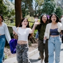 Four women waving to camera while walking on campus