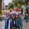 Five people wearing SF State Gators football jerseys and blue jeans stand on Malcolm X Plaza on an overcast and rainy day