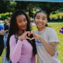 Two students make a heart shape with their hands with the Gator Giving Day logo pasted in the right side of the photo