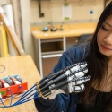 Lauren Gan wears and looks at robotic hand project