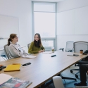 Three students and Michael Poryes laugh while seated at a table in a room in Marcus Hall with a window in the background