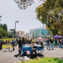 People walk across the Quad among tables on a sunny day