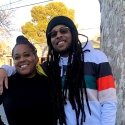 Marcus Angelo Bryant stands to the right of his mother, Theresa Thompson, with his right arm around her shoulders while both smile and stand next to a tree on a sunny day