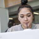 A woman sucks on a straw while looking at a laptop