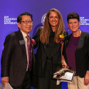 Three dressed up people pose together in front of a purple backdrop that says SFSU. 