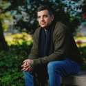 Man in olive green jacket and jeans sitting on a concrete bench.